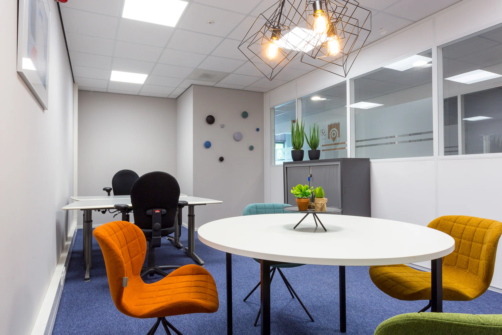 Moderne kantoorkamer aan de Niels Bohrweg met kleurrijke stoelen, witte tafels, planten en een geometrische hanglamp.